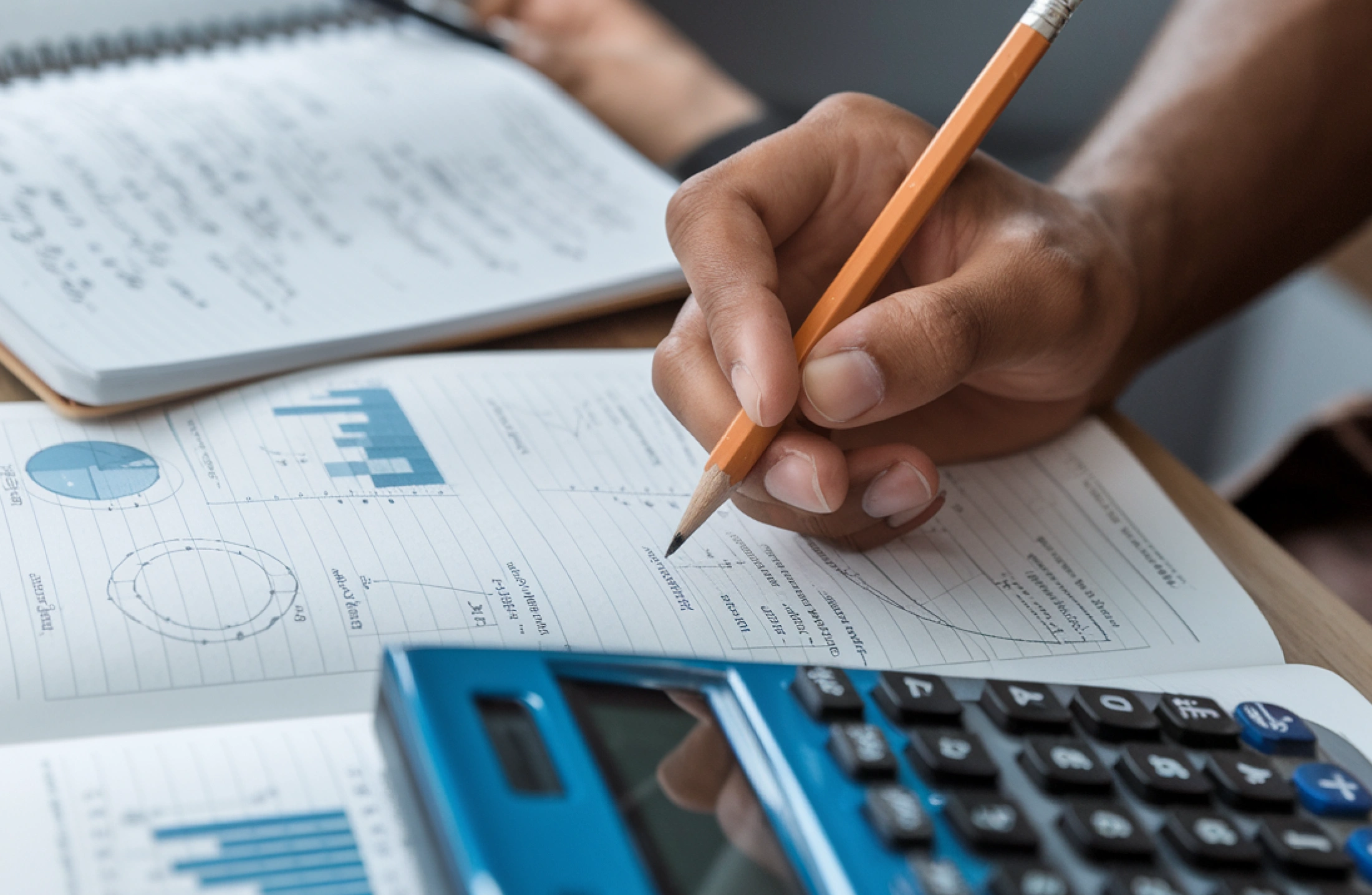 A student's hand holding a pencil and calculator